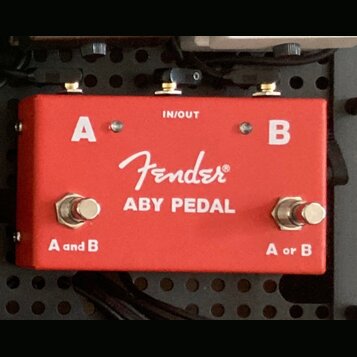 Červený kovový pedál s bílými nápisy. Uprostřed je logo Fender® a text ABY PEDAL, v horní části nápis IN/OUT a písmena A a B. Na spodní straně jsou d…