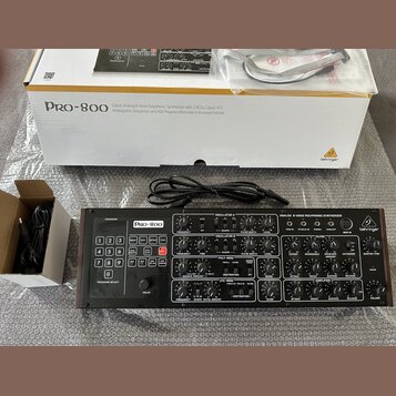 Černý analogový polyfonní syntetizátor s nápisem Pro-800 a logem Behringer. Přístroj obsahuje řadu potenciometrů, tlačítek pro výběr programů a ovlád…