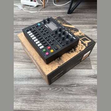 Černý digitální sekvencer a syntetizátor s nápisem Digitone, umístěný na originální krabici s nápisy Digitone a FM digital drum machine. Zařízení má…
