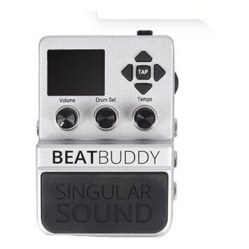 Stříbrný kytarový pedál s digitálním displejem a třemi ovládacími knoflíky označenými Volume, Drum Set a Tempo. V pravé horní části jsou čtyři směrov…