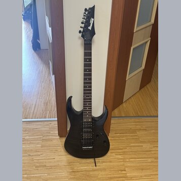Černá elektrická kytara s prořezaným povrchem těla a hnedý hmatníkem. Na hlavě je bílý nápis Ibanez. Nástroj má dva humbuckery, jeden ovládací knoflí…