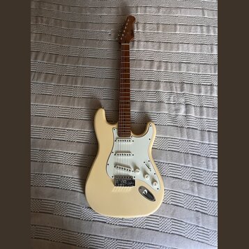 Elektrická kytara typu Stratocaster v krémové barvě s bílým pickguardem a hnědým hmatníkem. Na hlavě krku je viditelné logo "Squier". Nástroj má tři…
