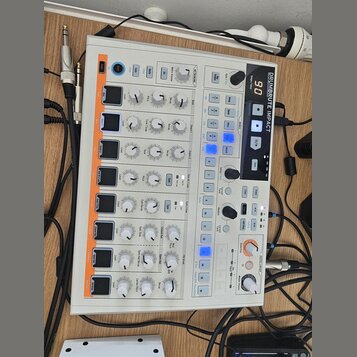 Bílá drum machine s názvem DRUMBRUTE IMPACT. Zařízení obsahuje řadu otočných potenciometrů, tlačítek a digitální displej s číslem 90. Na panelu jsou…