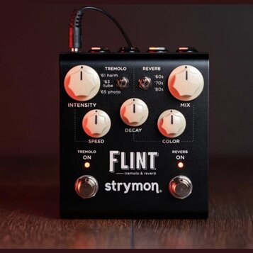 Černý efekt pedál s bílými ovládacími knoflíky. Na předním panelu jsou nápisy TREMOLO, REVERB, INTENSITY, MIX, SPEED, DECAY a COLOR. Uprostřed je vel…