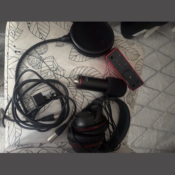 Sada audio vybavení položená na vzorovaném podkladu. Obsahuje červený zvukový interface s nápisem Scarlett 2i2, černý mikrofon s nápisem Scarlett, če…