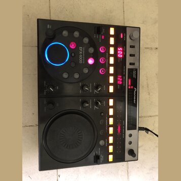 Černý DJ efektový procesor a kontrolér značky Pioneer s označením EFX-1000. Zařízení obsahuje velký ovládací disk s modrým podsvícením, několik menší…