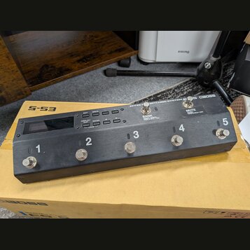 Černý efektový spínač s pěti stoupacími spínači označenými čísly 1 až 5. Na horní části je nápis EFFECT SWITCHING SYSTEM ES-5 BOSS, displej a ovládac…