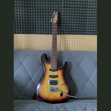 Elektrická kytara s trupem v barevně sunburst a hnedým hmatníkem. Na hlavě je vidět nápis Ibanez. Nástroj má dva humbuckery, jeden jednosmykový sníma…