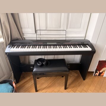 Černý digitální piano s klaviaturou a přívodním kabelem, umístěný na černém stojanu. Na levé straně je nápis MEDELI a vpravo označení PIANO 100. Před…