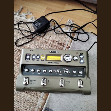 Šedo-zelený looper s nápisy LINE 6 a JM4 Looper. Zařízení obsahuje řadu ovládacích knoflíků, tlačítek a malý displej s textem STYLE: EASY. Ve spodní…