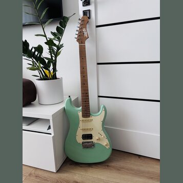 Světle zelená elektrická kytara typu Stratocaster s bílým pickguardem a hnědým hmatníkem. Na hlavě nástroje je bílé logo "Squier". Kytara má konfigur…