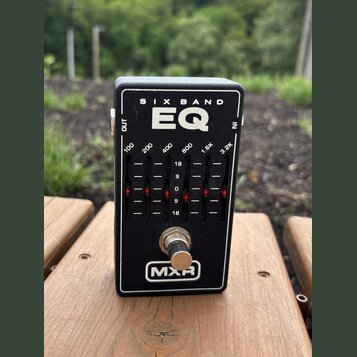 Černý efekt pedál s nápisy SIX BAND a EQ. Na panelu jsou označení frekvencí 100, 200, 400, 800, 1.6K a 3.2K s posuvníky a stupnicí od 18 do 18. V dol…