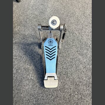 Fotografie znázorňuje bicí pedál s modrou kovovou plošinkou a stříbrným šlapadlem. Na plošince je umístěno logo a nápis YAMAHA s černým grafickým vzo…