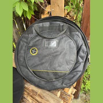 Černý kulatý polstrovaný obal na hudební nástroj s rukojetí. Na přední straně je kulatý štítek s nápisem ROCKBAG a textem "ROCKBAG by THE MUSIC GROUP…