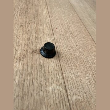Černý plastový knoflík s kulatým základním tvarováním. Na spodní části je viditelný nápis G. l. 01 a písmeno R. Povrch vykazuje mírné známky opotřebe…