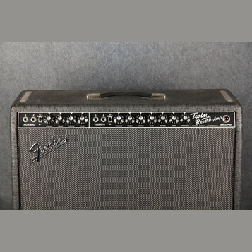 Kytarový kombozesilovač v černém potahu s textilní maskou. Na ovládacím panelu jsou nápisy NORMAL, VIBRATO a Twin Reverb-Amp, dále značka FENDER MUSI…