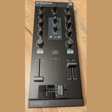 Černý DJ kontrolér s nápisy TRAKTOR a KONTROL Z1. Zařízení obsahuje několik otočných knoflíků, posuvníky hlasitosti pro kanály A a B, crossfader a tl…