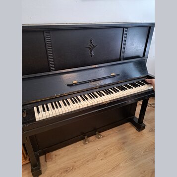 Černé akustické piano s klaviaturou z bílých a černých kláves. Na přední části nad klaviaturou je nápis AKORD v oválném rámečku a v horní části korpu…