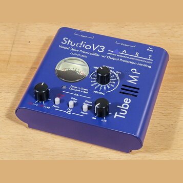 Modrý předzesilovač s nápisy StudioV3, ART a Voiced Valve Preamplifier w/ Output Protection Limiting. Zařízení má analogový VU metr, dva černé oválné…
