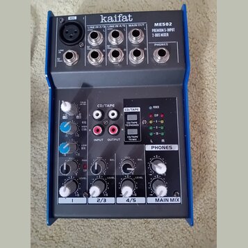 Kompaktní mixážní pult s modrým kovovým rámem a šedým předním panelem. Na horní části jsou nápisy kaifat, ME502 a PREMIUM 5-INPUT 2-BUS MIXER. Zaříze…
