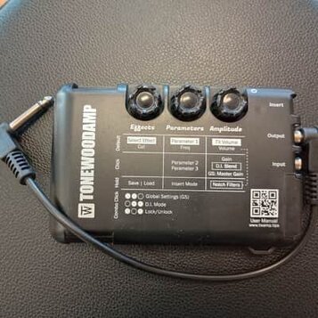 Černý efektový pedál s nápisem TONEWOODAMP. Na horní straně jsou tři černé ovládací knoflíky a tabulka s popisy funkcí Effects, Parameters a Amplitud…