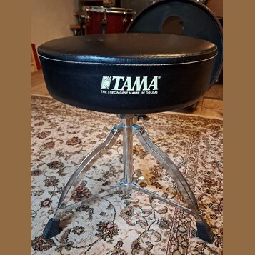 Černý polstrovaný bubeníckýstoliček s chromovaným trojnožným stojanem. Na boku sedáku je bílý nápis TAMA a pod ním text THE STRONGEST NAME IN DRUMS.…