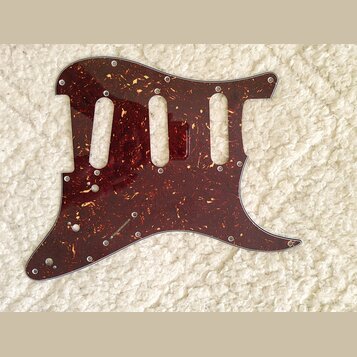 Tmavě červený pickguard s texturou želvy (tortoise shell) určený pro elektrickou kytaru. Má tři vyřezané otvory pro snímače a několik otvorů pro šrou…