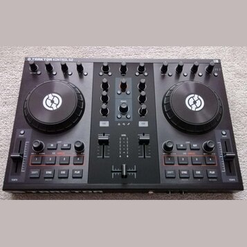 Černý DJ kontrolér s nápisem TRAKTOR KONTROL S2 v levém horním rohu. Zařízení má dva velké jog-kola s bílým logem, zahlreichetočítka a posuvníky. Pov…