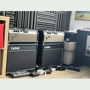 Dvě kytarové komba značky Fender umístěná na dvou černých kytarových boxech značky Laney. Komba mají stříbrný přední panel s nápisy Fender a v pravém…