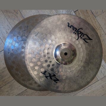 Dvě mosazné činely s viditelným rýhováním a kovem s hammered efektem. Na horním činele je nápis Zildjian, model ZXT a označení Rock Crash Ride 18". P…