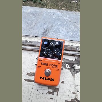Oranžový kytarový efekt pedál s nápisy TIME CORE DELUXE a NUX. Horní panel obsahuje čtyři ovládací knoflíky s popisky Time, Mix, Reverse Mod a Repeat…