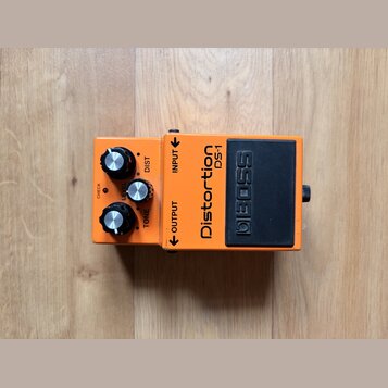 Oranžový efekt pedál s černým spínacím tlačítkem. Na zařízení jsou nápisy Distortion DS-1 a BOSS, dále popisky ovládacích prvků DIST, LEVEL a TONE a…