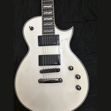 Bílá elektrická kytara s tvarem připomínajícím Les Paul a bílým lemováním kolem korpusu. Nástroj je vybaven dvěma černými humbuckery s oranžovým nápi…