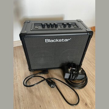 Černý kytarový kombo zesilovač s nápisem Blackstar na přední textilní mřížce. Horní ovládací panel obsahuje několik otočných potenciometrů a přepínač…