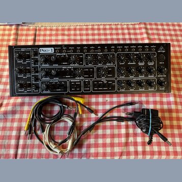 Černý analogový synthesizer s nápisy PRO-1 a behringer. Přední panel obsahuje zahlreiche ovratidla, přepínače a konektory s popisy jako OSCILLATOR A,…