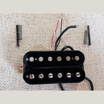Černý humbucker s dvěma řadami snímačů, z nichž horní má hladké krytky a spodní šroubovací. Z nástroje vedou červený, bílý a několik černých vodičů.…
