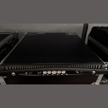 Černý rackový přístroj v transportním kufru s hliníkovými hranami. Na přední hraně je vidět ovládací panel s bílými tlačítky, USB portem a logy v pod…