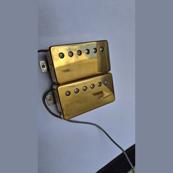Dva humbuckery s gold povrchem a viditelnými šrouby v polosách. Povrch vykazuje drobné škrábance a známky opotřebení. Z obou snímačů vedou šedé vodič…