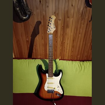 Elektrická kytara s trupem v barevném přechodu od černé přes červenou k žluté a bílým pickguardem. Na hlavě hmatníku je vidět nápis STRATOCASTER. Nás…