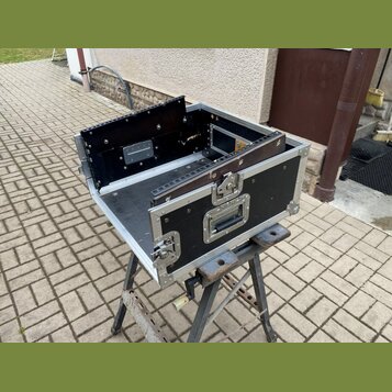 Černý transportní flightcase s hliníkovými hranami a vrchním víkem otevřeným do strany. Uvnitř jsou vidět montážní lišty pro rackové zařízení a kovov…