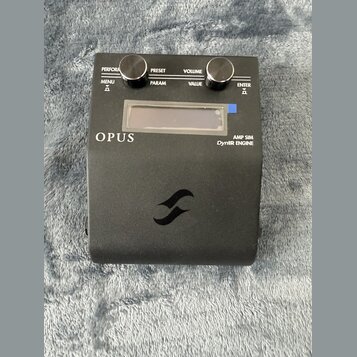 Černý kytarový pedál s nápisy OPUS, AMP SIM a DynIR ENGINE. Horní panel obsahuje dva černé oválné knoflíky a nápisy PERFORM, PRESET, VOLUME, MENU, PA…