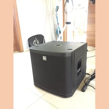 Černý subwoofer s hranatým tvarem a přední kovovou mřížkou. Na mřížce je umístěno bílé logo "EV". Povrch je v matném provedení, horní strana obsahuje…