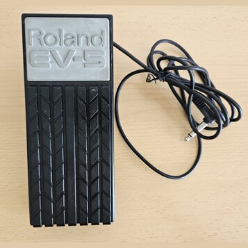 Černý expresní pedál s gumovou protiskluzovou texturou v podobě ševronů. Na horní části je šedý panel s vyraženým nápisem Roland EV-5. K zařízení ved…