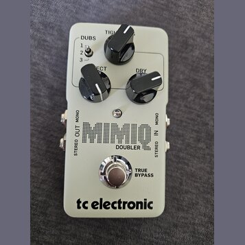 Šedý kytarový efekt s nápisem MIMIC DOUBLER a logem tc electronic. Na horní části jsou tři černé otočné ovladače s popisky TIGHT, ECT a DRY a přepína…