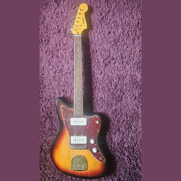 Elektrická kytara s trupem v přechodovém žlutě-červeném odstínu a hnědým hmatníkem. Na hlavě je nápis Squier by Fender. Kytara má červený vzorovaný p…