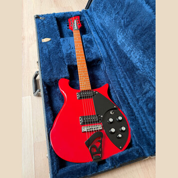 Červená elektrická kytara v černém tvrdém kufru s modrým plyšovým vnitřkem. Na hlavě hmatníku je bílý nápis Schecter. Kytara má dva černá humbuckery,…