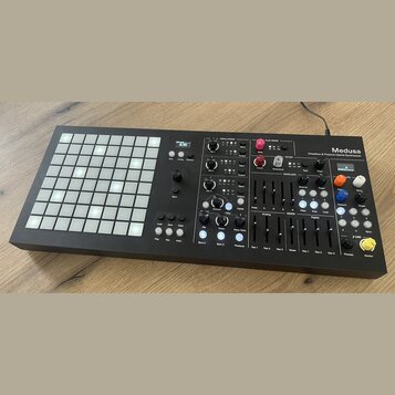 Černý hybridní syntetizátor s nápisem Medusa a podtitulem Dreadbox & Polyend Hybrid Synthesizer. Na levé straně se nachází mřížka bílých podsvícených…