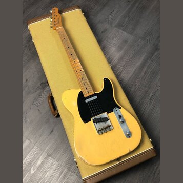 Žlutá elektrická kytara typu Telecaster položená na žlutém tvrdém kufru. Na hlavě hmatníku je viditelný nápis Fender. Kytara má černý pickguard, jede…