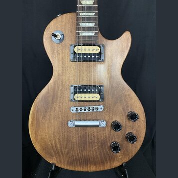 Elektrická kytara s hnědým dřevěným povrchem a dvěma humbuckery. Na přepínači je nápis TREBLE. Kytara má čtyři černé oválné knofíky a stříbrný most s…