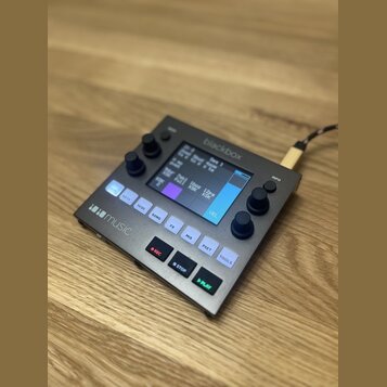 Kompaktní černý sampler s displejem a ovládacími prvky. Na horní hraně je nápis blackbox, v levém dolním rohu logo 1010music. Zařízení obsahuje někol…